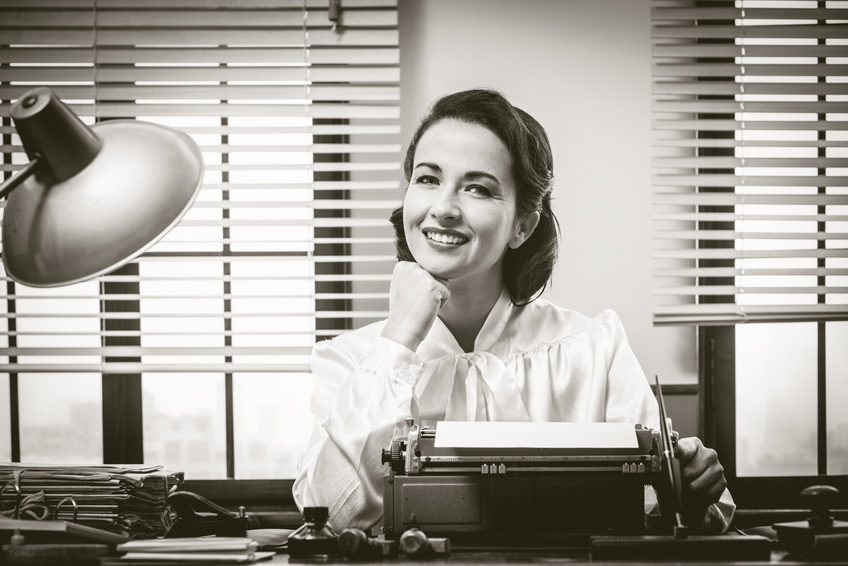 1950s style secretary working at office desk and smiling with hand on chin | Blogger